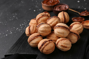 Wall Mural - cutting board with sweet walnut shaped cookies with boiled condensed milk on black background