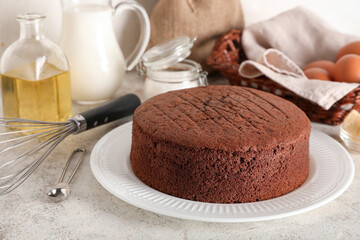 Wall Mural - delicious chocolate sponge cake with ingredients and whisk on light grunge background