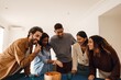 © Drobot Dean - A multiethnic group of five friends laughs around a table, sharing snacks. Latino, Black, and Asian people enjoy chips from a bowl. A young Indian woman in a blue shirt points at a table.