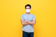 © Atstock Productions - Casual young Asian man wearing face mask and looking at camera with arms crossed on isolated yellow color background studio shot