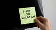 © Anom S. - Hand attaching a vacation notice on a computer monitor in the office