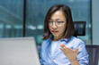 © Liubomir - Focused and serious businesswoman talking to colleagues and partners using laptop and video call. Confident Asian office worker close up on online business meeting conference.