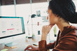 © deagreez - Young professional woman working in an office with natural light and modern design, analyzing data on her computer screen
