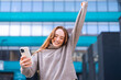 © Iryna - Woman celebrating with joy outdoors while looking at her smartphone in an urban setting during daytime