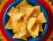 © S-DESIGN - A blue bowl of tortilla chips sitting on a brightly colored table runner. The chips are crispy and golden brown, perfect for dipping or snacking. They are arranged in a pile.