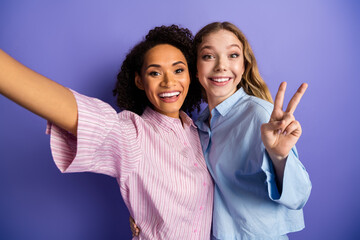 young female friends taking a cheerful selfie against a purple background while celebrating together