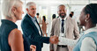 © Jessy/peopleimages.com - Conference, handshake and meeting with business people at event for global forum, investor summit and networking. Welcome, b2b convention and expo with employees in lobby for brand exposure seminar