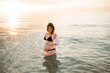 © morrowlight - Pregnant woman wearing black swimsuit in sea water over sunset outdoors. Summer vacation time. Maternity.