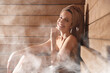 © New Africa - Smiling woman relaxing surrounded by steam in sauna