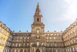 Visitors admire the stunning architecture of Christiansborg Palace in Copenhagen, surrounded by historical charm under a bright blue sky. The grandeur of this government building captivates all.