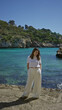 © Krakenimages.com - Woman smiling in white outfit enjoys sunny day by the turquoise waters and rocky cliffs at santanyi beach in mallorca with lush greenery surrounding the mediterranean landscape.