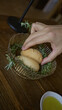 © Krakenimages.com - Hand reaching for bread in a rosemary-lined bowl on a wooden table in a mediterranean restaurant setting with a dish of olive oil nearby, showcasing rustic dining elegance.
