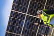 © ultramansk - Technician inspects solar panels under a large solar carport structure. Focused on clean energy, and sustainability, Engineer in safety vest and helmet pointing towards a solar powered carport.