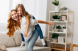 © SHOTPRIME STUDIO - Mother and daughter laughing and playing on a cozy couch in a bright, cheerful living room