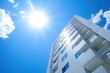 © Rahman - Modern apartment building under a bright sunny sky.  The building's facade is clean and white, showcasing balconies and windows.  Clear blue sky with puffy white clouds and a prominent sun