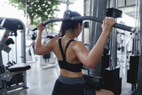 Young sportswoman training back muscles using lat pulldown machine in a modern fitness center, promoting a healthy and active lifestyle through strength training