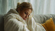 © Inspire Shots Hub - Woman wrapped in fluffy white blanket, sitting on sofa, head down, conveying sadness or contemplation