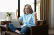 © Maria Vitkovska - Excited senior woman celebrating online success with laptop at home