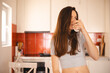 © zvkate - Young pretty cheerful brunette long hair woman is drinking a glass of water in home kitchen in the morning. Happy laughing girl, daily drink habit, hydration, morning routine.