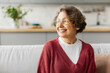 © Home-stock - Happy grey-haired senior woman sitting on couch at home and looking aside at free space with smile, enjoying domestic pastime
