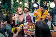 © Lomb - Group of friends laughing and toasting at outdoor dinner party with lights and food
