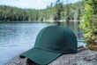 © DigitalFrame - Forest green baseball cap mockup displayed on rock by a calm lake in natural outdoor setting