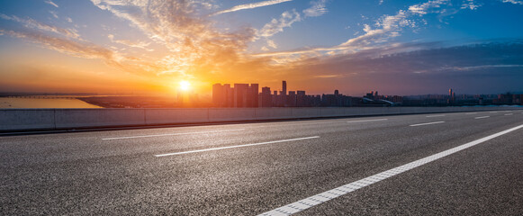 Wall Mural - empty asphalt road with the cityscape at sunrise