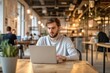 © Harsha - Young man works on laptop in a modern coworking space with a blurred background.