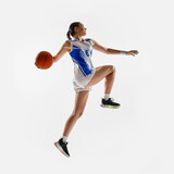 Slam dunk. Side view photo of young fit girl, basketball athlete leaping in mid air to get score against white background. Concept of professional sport, woman in sport, movement, fitness. Ad