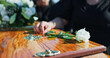 © peopleimages.com - Coffin, flower and hand at memorial with respect, grief or loss at family service for burial. Person, mourning and grieving relative with white rose on casket for remembrance at funeral at graveyard.