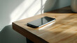 © Lucianastudio - Modern mobile phone resting on a wooden surface in a pool of sunlight creating a peaceful ambiance