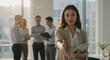 © schiers_images - Confident businesswoman with curly hair extends a handshake in a modern office space, teamwork and collaboration visible. Background features professionals working alongside her