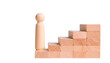 © photostockatinat - a wooden figure standing at the base of a staircase made of wooden blocks, a metaphor for progress