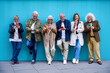 © CarlosBarquero - Group of senior people using technology devices together online leaning on blue wall. Joyful mature friends having fun watching social networks on mobile phones. Tech and modern old concept
