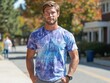 © Supriyati Pixxel - A young man with blond hair and a beard smiles gently, wearing a tie-dye shirt, while walking outdoors on a sunny day
