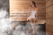 © New Africa - Beautiful woman relaxing on wooden bench surrounded by steam in sauna