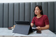© crizzystudio - Asian freelancer woman working on a tablet in a cozy cafe, savoring a cup of coffee and indulging in a delicious blueberry cheesecake while holding a notebook in her hand