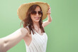 © Vladimir Razgulyaev - Woman 30- 35 years old female tourist traveler in a wide-brimmed hat takes a selfie against a light green background portrait isolated. The concept of solo travel or advertising summer tours.
