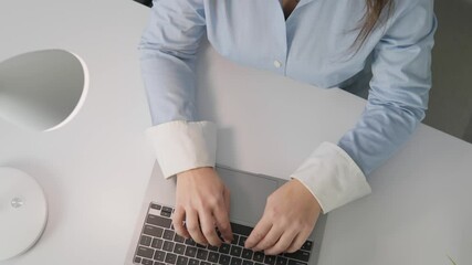 Poster - A dedicated woman wearing a light blue blouse is working intently on her laptop at a stylish desk adorned with a chic lamp, clearly demonstrating her intense focus and high level of productivity