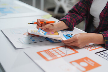 Wall Mural - web designer is holding a pen and reviewing mobile application wireframes and prototypes, adding not