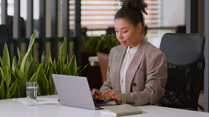 Serious ethnic woman African American girl businesswoman female employer broker agent lady business worker manager look at laptop pc screen work online computer studying learning e-commerce at office