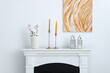 © New Africa - Stylish candlesticks with burning candles and other decor on fireplace near white wall indoors