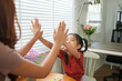 © PRIME STOCK LAB - Happy child and adult giving high five while sitting at table near window blinds in bright room