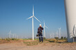 © kelvn - Engineer wearing uniform inspection and survey work in wind turbine farms rotation to generate electricity energy. Maintenance engineer working in wind turbine farm at sunset.