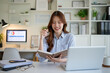 © wattana - Young businesswoman writing in notebook while working on laptop at home office.