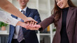 © wattana - Close-up of businesspeople placing hands together in a teamwork gesture, symbolizing unity, collaboration, and shared success.