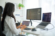 © wattana - Woman using external keyboard and stylus, programming across a three-screen workstation in home office.