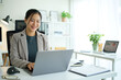 © wattana - Young businesswoman in a blazer enjoying remote work, typing on a laptop at a bright desk with documents and charts.