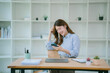 © PSG - Happy young asian woman talking on the mobile phone and smiling while sitting at her working place in office.