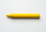 A close up shot of a single yellow crayon lying horizontally on a white surface in a studio setting
